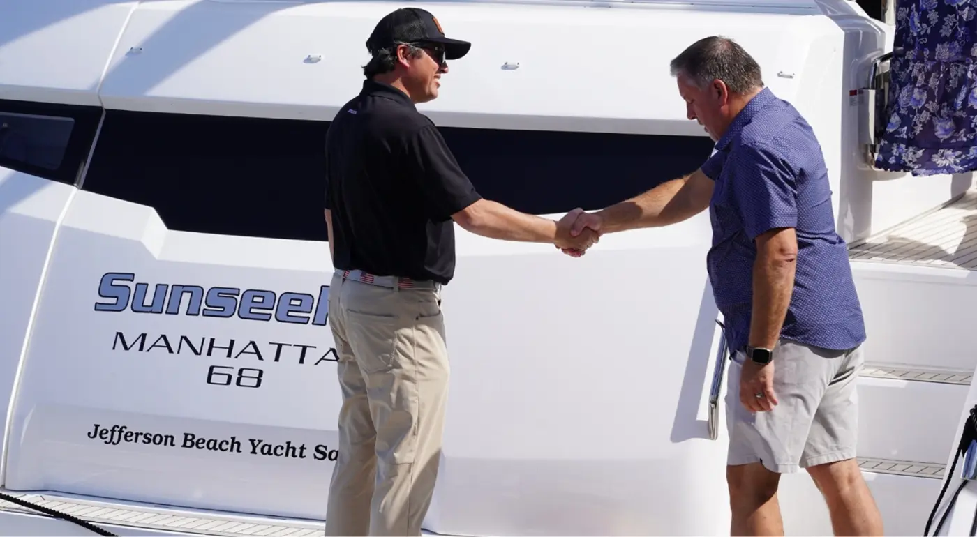 Two men shaking hands while purchasing a yacht.