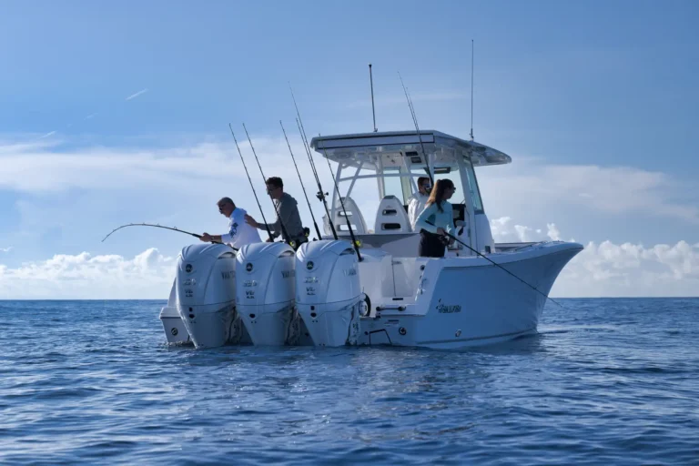 White sportfishing boat with multiple fishing rods and several anglers fishing from the stern on a calm blue ocean surface.
