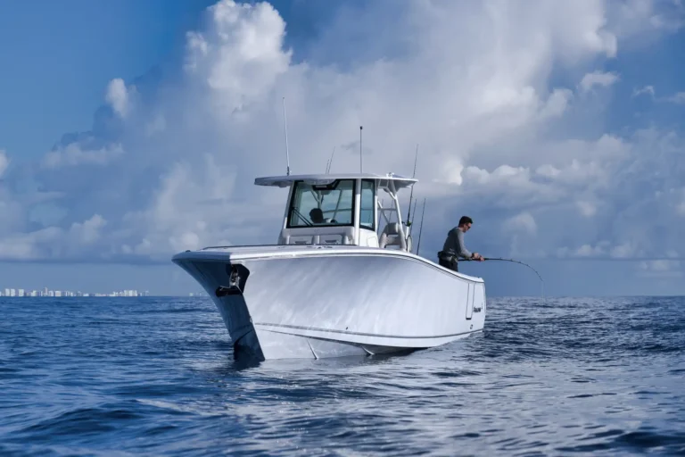 Man fishing from the side of a white cabin cruiser on a calm blue sea under a partly cloudy sky.