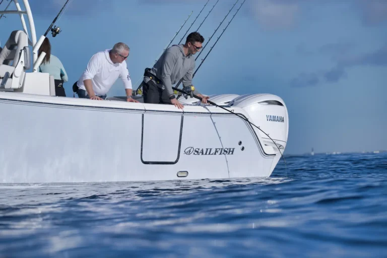 Three people stand on a white Sailfish fishing boat, leaning over the railing with fishing rods ready at sea with a Yamaha outboard engine visible on the stern.