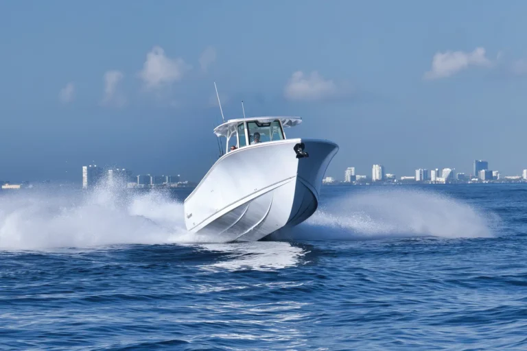 White motorboat speeds across blue water, spray trailing as a city skyline rises in the distance.