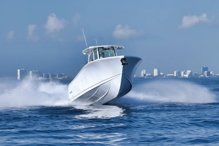 White motorboat speeding across choppy blue water with a city skyline in the distance.