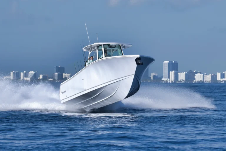 White speedboat surging through blue water with a city skyline in the background.