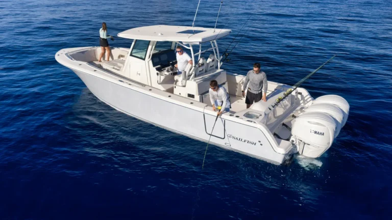 White sport fishing boat with four people on a deep blue sea, two at the stern fishing rods deployed and one person at the captain's console inspecting gear
