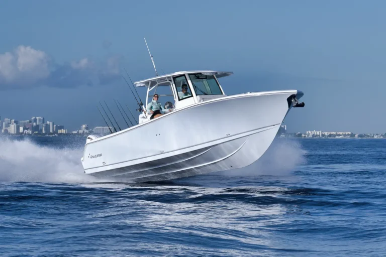 White sport boat bursting through water at high speed with two people on board and a city skyline in the distance