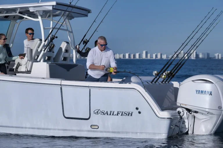 People fishing from a white yacht named Sailfish, with multiple rods secured at the stern and a Yamaha motor in the foreground against a city skyline.