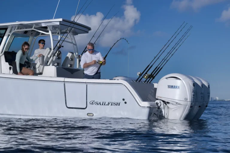 White sport fishing boat with six rod holders and three anglers preparing gear under a blue sky.