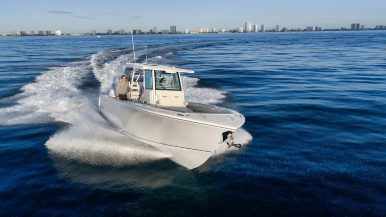 White speedboat cutting through calm blue water with a coastal city skyline in the distance.