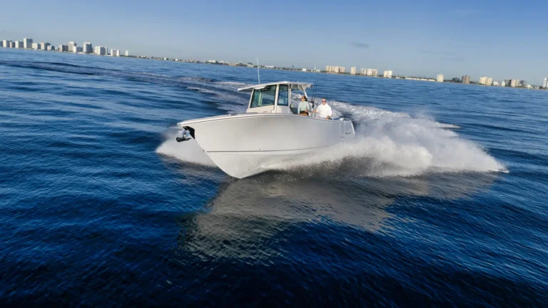 White motorboat speeding across blue ocean with two people on board and city skyline in the background, modern high-rises along the shore, clear sky.