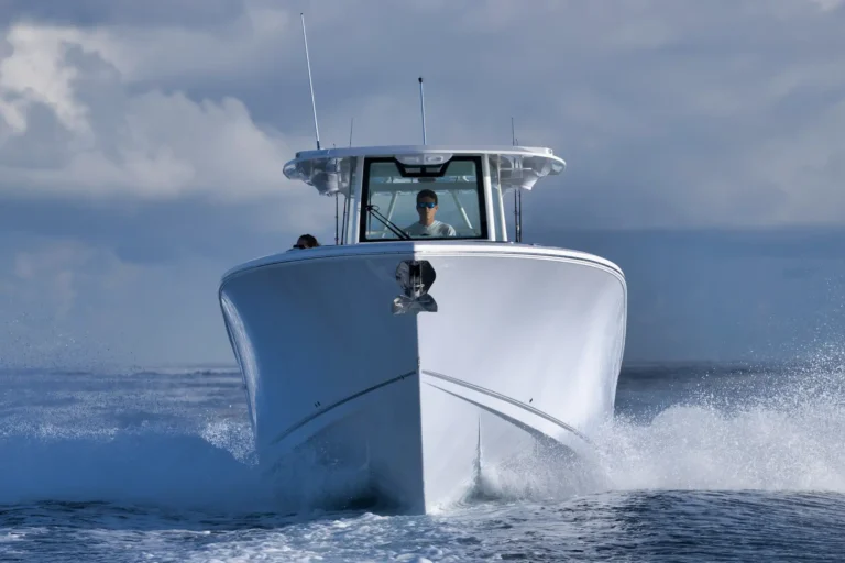 Front view of a white motorboat speeding through choppy water; a person in the helm wears sunglasses.