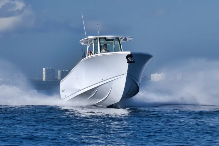 Powerful white motorboat cutting through choppy water with a distant city skyline in the background, two people visible in the cabin.