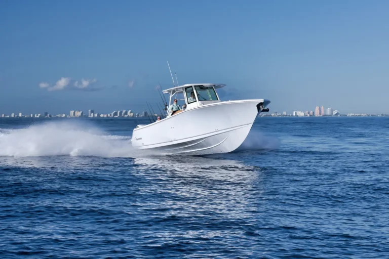 White motorboat speeding across blue ocean with a city skyline visible on the horizon.