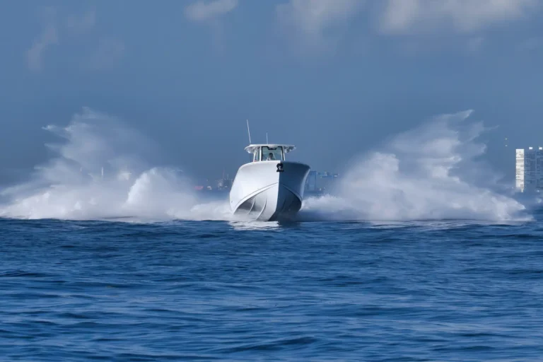 White speedboat slicing through blue ocean as waves splash, city skyline on the horizon behind it.