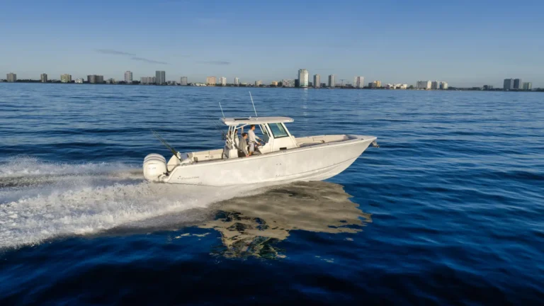 White motorboat speeding across calm blue water with a city skyline in the background; wake rippling behind the boat.