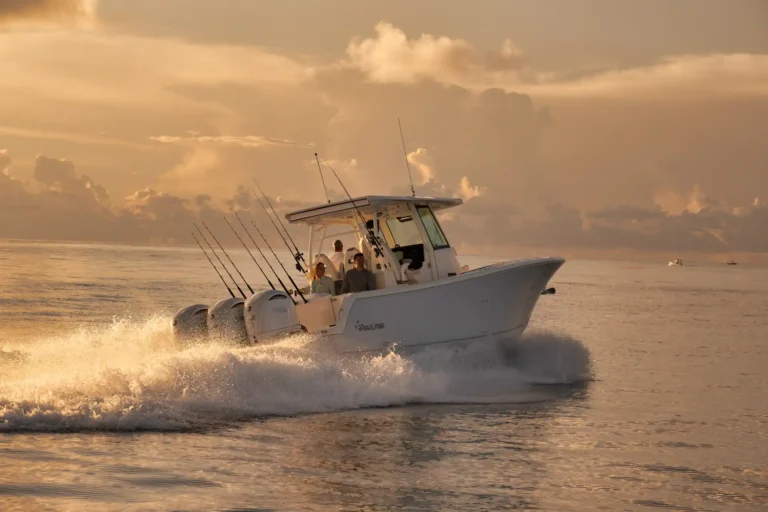 White sport fishermen's boat speeding across calm water at sunset, with several fishing rods mounted along the stern.