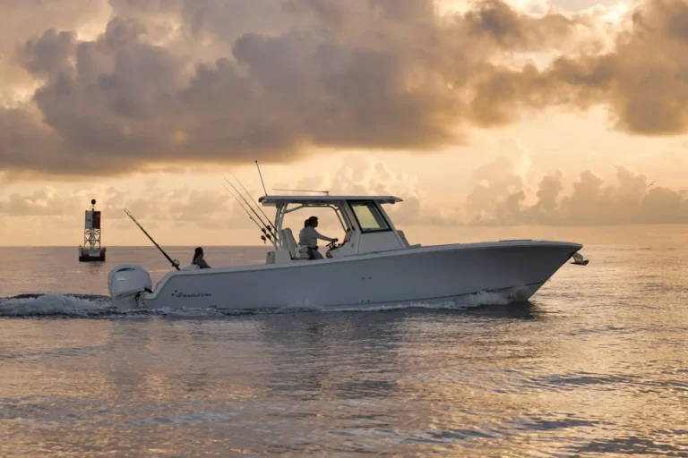 White motorboat cruising on calm water at sunset, fishing rods attached to the stern and two people on board under a cloudy, golden sky