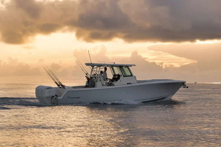 White sport fishing boat with several fishing rods on the stern, cruising at sunset over calm water.