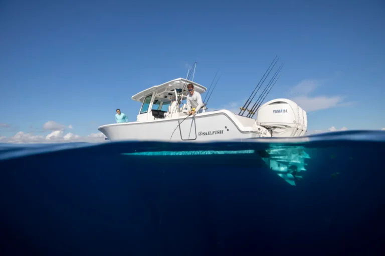 Over-and-under shot of a white Sailfish fishing boat on blue water; two men on deck with fishing rods and a Yamaha outboard visible at the stern.