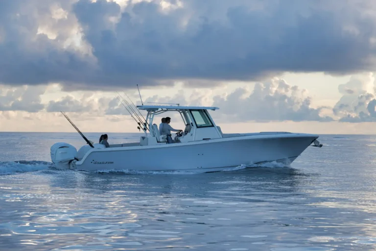 White fishing boat with two people aboard, fishing rods ready, gliding across calm blue water under a cloudy sky.