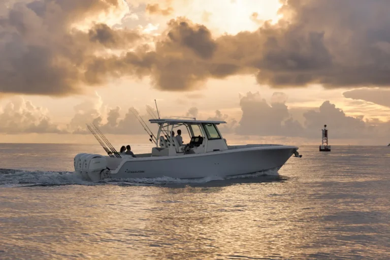 White sportfishing boat on calm ocean at sunset with fishing rods upright and dramatic clouds above.