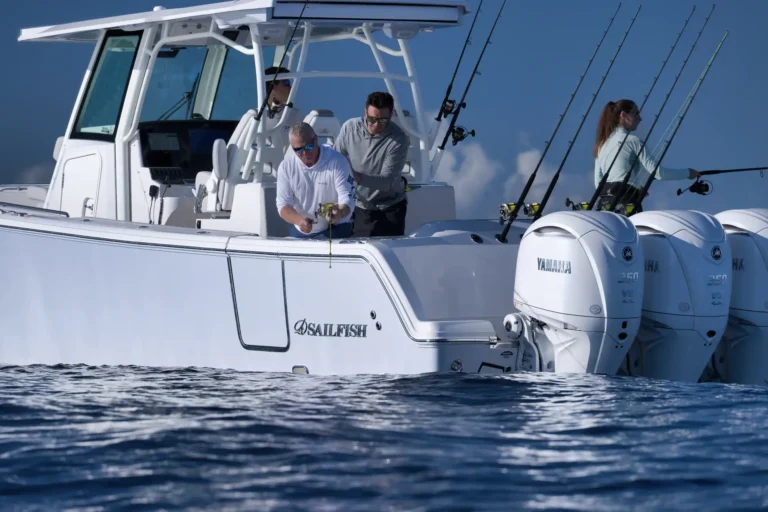 White sportfishing boat with multiple rods in holders, two men and a woman preparing gear on the deck; Yamaha engines in background