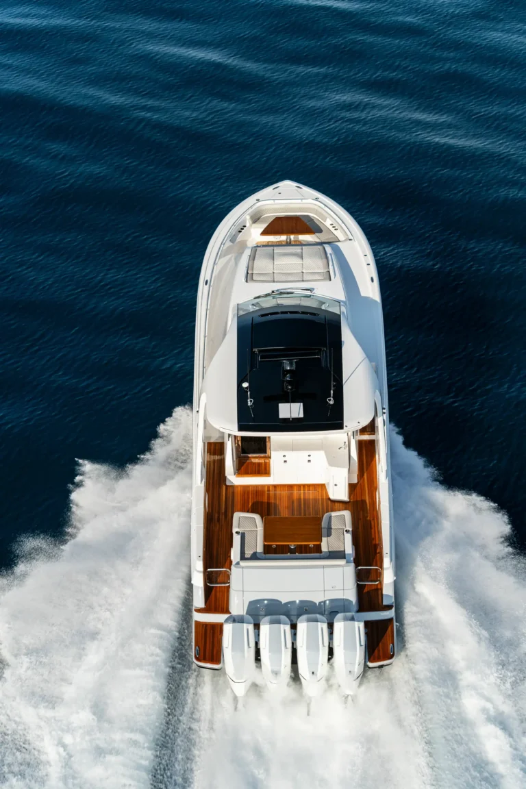 Top-down view of a white luxury motor yacht speeding through deep blue water with a foamy wake behind it.
