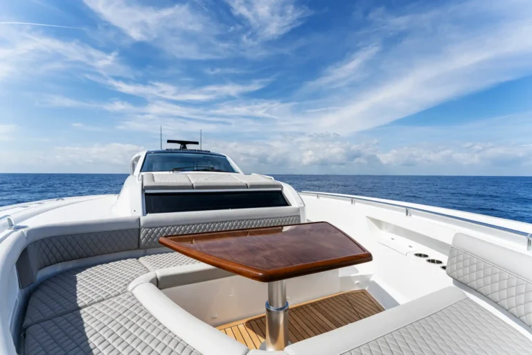 White luxury yacht deck seating area with quilted cushions and a wooden table overlooking the sea