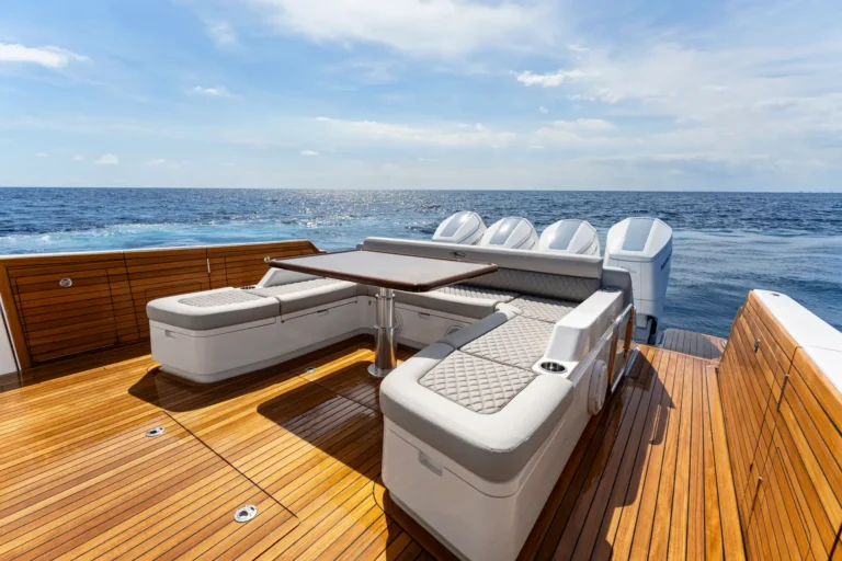 Wooden deck of a luxury yacht with white cushioned seating, a teak table, and the ocean in the background.