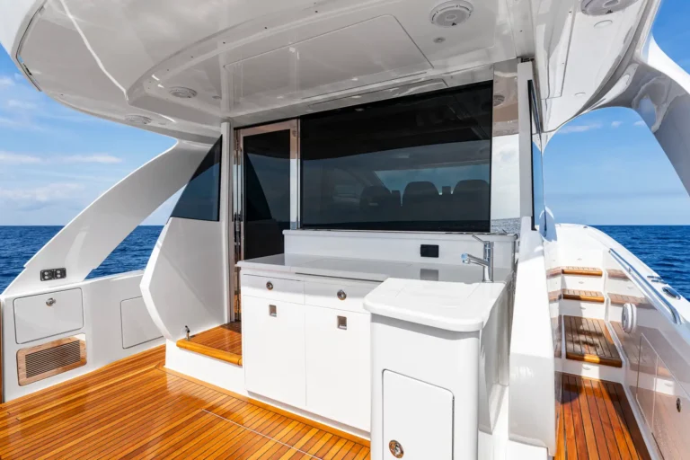 Outdoor yacht galley with white cabinetry, sink, and a large flat-screen TV, teak deck and blue ocean backdrop.