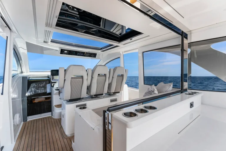 Luxurious yacht interior with row of white captain chairs, open skylight, and blue sea visible through large windows.