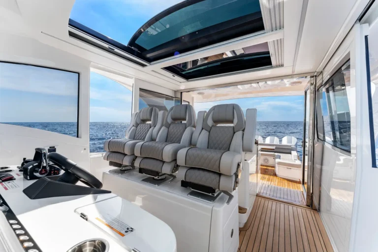 Luxurious boat cockpit with multiple gray captain-style seats, open sunroof, and ocean view through windows and doorway to deck.