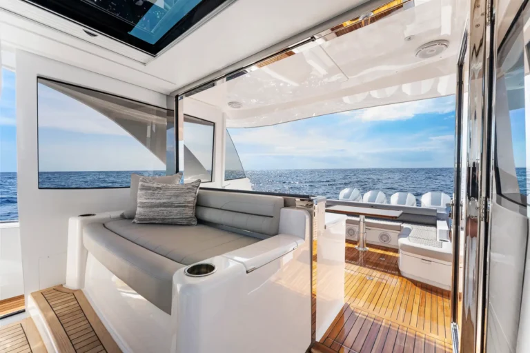 Luxurious yacht seating area with gray cushions and large ocean view through glass walls and doors.
