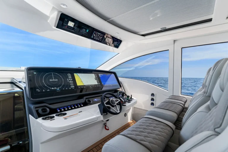 Modern yacht cockpit with large navigation screens, steering wheel, and an ocean view through expansive windows.