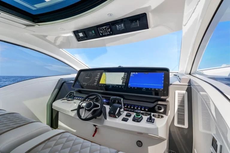 Modern boat cockpit with a large touchscreen chartplotter, steering wheel and control panels, ocean visible through the windows outside.