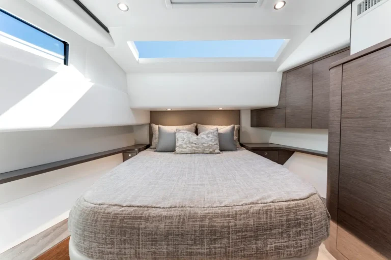 Cosy boat cabin with a large bed, neutral bedding, and dark wood cabinets along the right wall under a skylight panel.