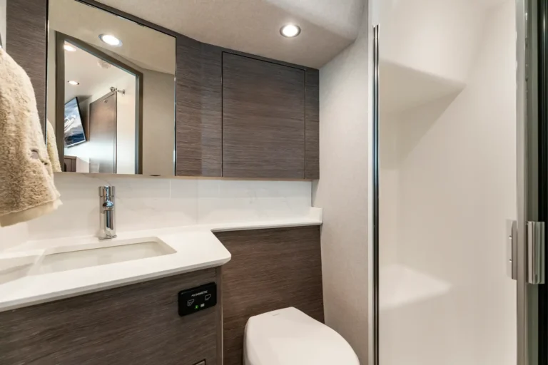 Modern bathroom with dark wood vanity and wall cabinets, white sink, chrome faucet, towel on the left, and glass shower door.