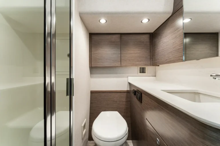 Modern bathroom with a white toilet, dark wood vanity, white countertop, and glass shower on the left.