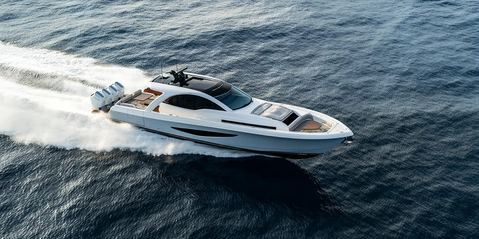 Aerial view of a white luxury speedboat cruising on open water, leaving a foamy wake behind.