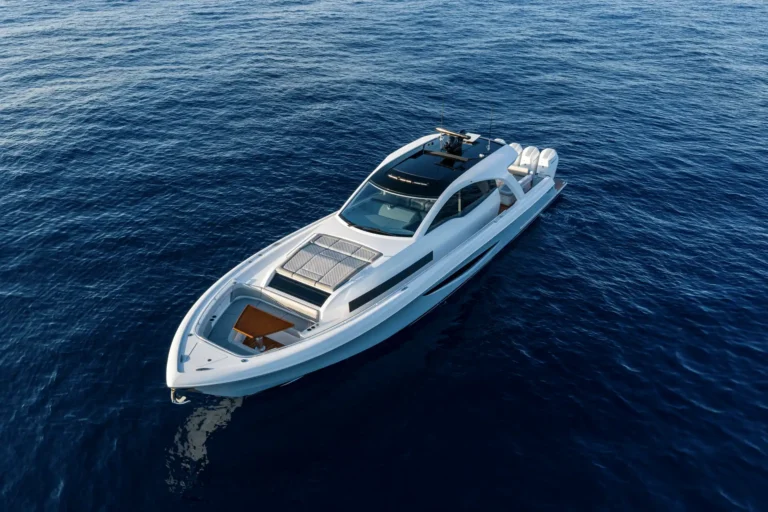 Aerial view of a white luxury motor yacht cruising on deep blue open water with sunlit reflections on the waves.