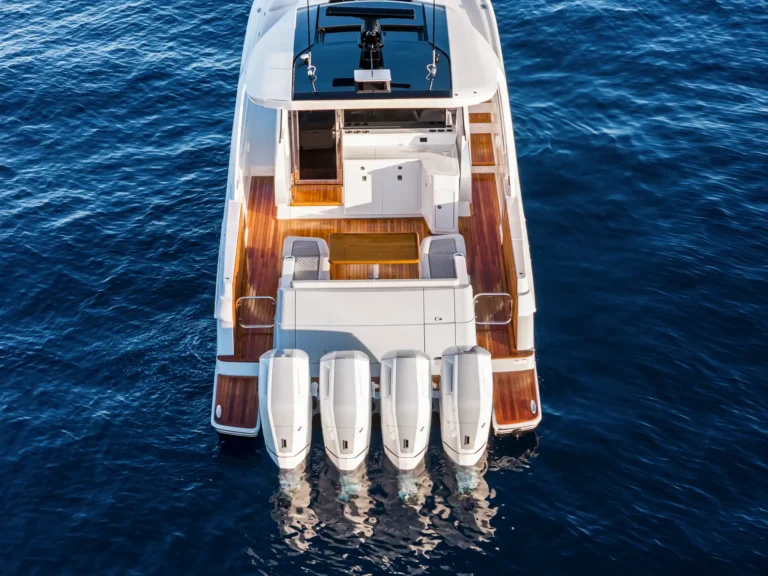 A top-down view of a white luxury motor yacht with multiple outboard engines at the stern and teak decking on blue ocean water.