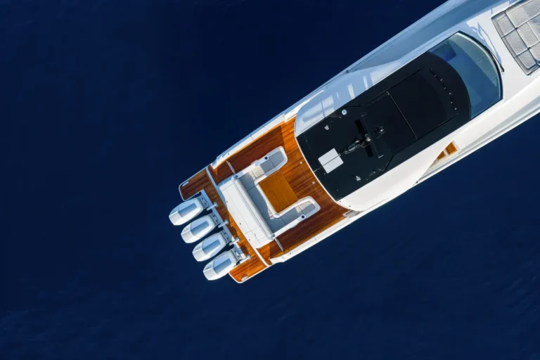 Top-down aerial view of a luxury white yacht with teak deck sailing on deep blue water