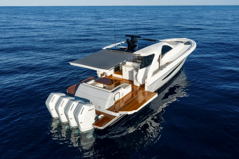 Overhead view of a sleek white luxury motorboat floating on calm blue sea with a teak deck and open stern area.