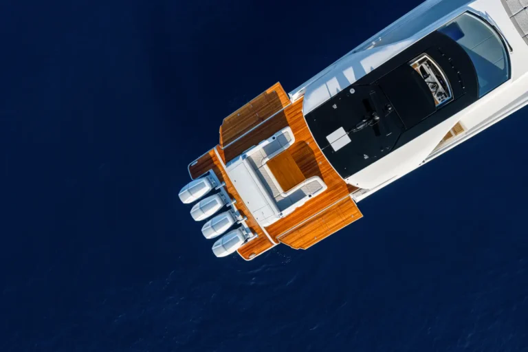 Top-down view of a luxury yacht bowing into deep blue water, highlighting teak deck and sleek white hulls