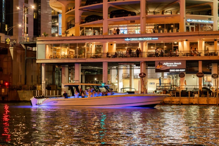 Nighttime waterfront with a multi-level restaurant building and a large yacht in the foreground; warm lights reflect on the water.