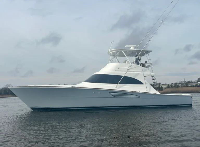 White sport yacht on calm water with tall fishing rods and a cabin, shoreline in background