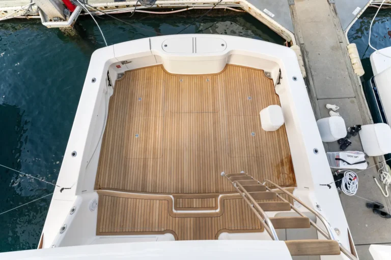 Top-down view of a yacht deck with teak flooring, white hull, and a dock beside the boat at the marina.