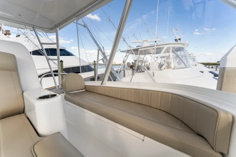 Open-air seating area on a yacht with tan cushions and a cup holder, marina with other boats in the background.
