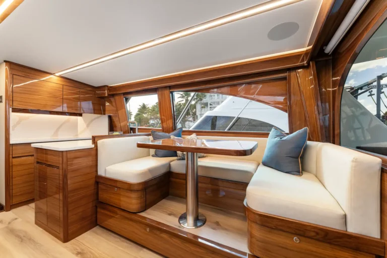 Luxurious wooden yacht salon with white upholstered seating, a round table, and large windows.