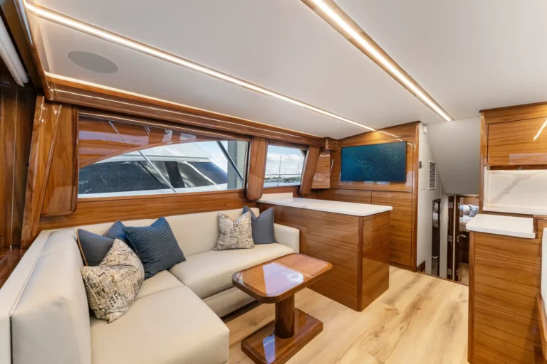 Luxurious yacht lounge with cream sofa and blue pillows, wood paneling, and a flat-screen TV on a wooden wall