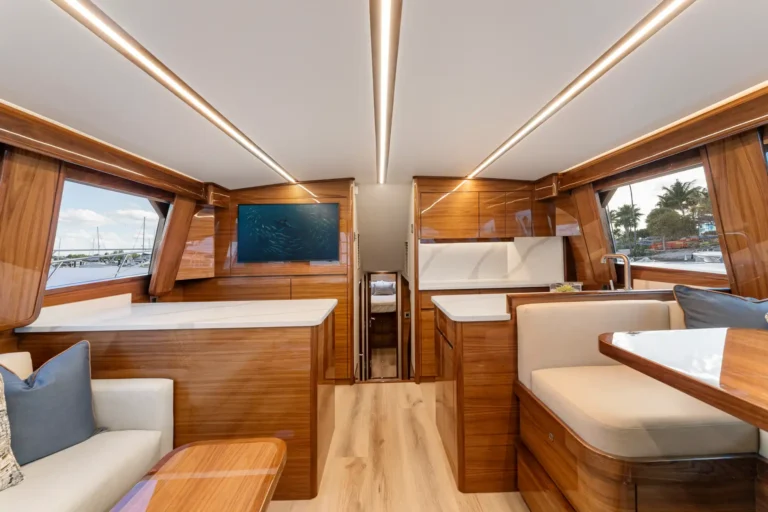 Interior of a luxury yacht: warm wood paneling, cream seating, white countertops, and large harbor-facing windows